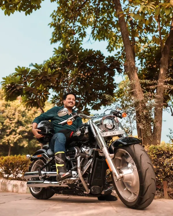 A portrait of a rider on his Harley Davidson Fat Boy. The low angle emphasizes the bike's powerful presence, while the natural, leafy background provides a great contrast to the chrome and black metal.