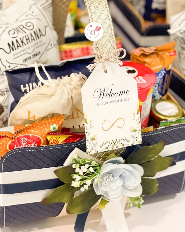 A close-up of our welcome room hamper, featuring a personalized "Welcome to our wedding!" tag, a mix of popular Indian snacks, and a touch of floral decoration.