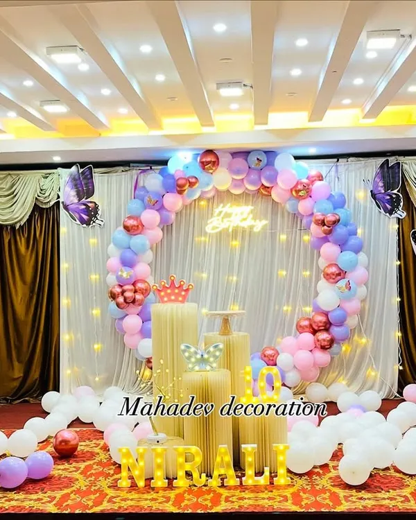 A stunning butterfly theme birthday party in a large hall. This setup features a circular balloon arch in pastel colors against a white curtain backdrop, with large purple butterfly cutouts on balloon pillars.