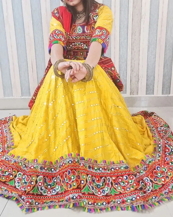 This is my most popular Navratri chaniya choli, perfect for dandiya nights. The bright yellow skirt is covered in mirror work and has a wide, colorful embroidered border that creates a beautiful flare when you twirl. The set includes the stitched blouse, skirt, and a matching red bandhani dupatta.