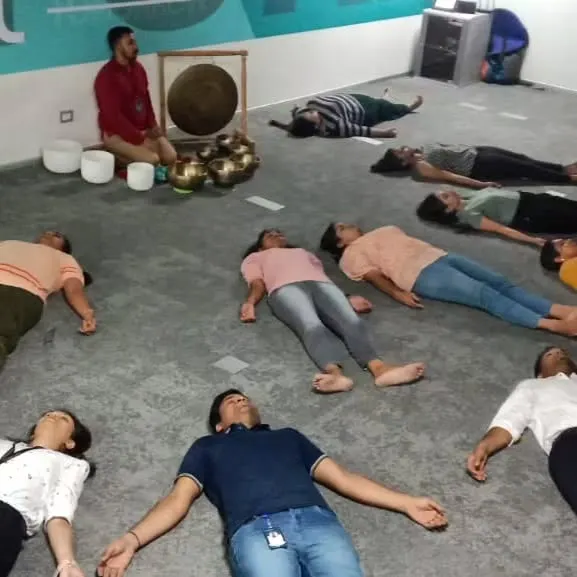 I create a sanctuary of calm right in your office space. Here, a team experiences a deep state of relaxation during a corporate sound meditation session, lying comfortably as the healing vibrations of singing bowls wash over them.