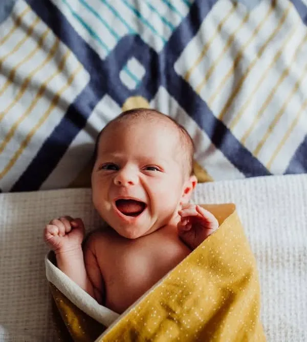 A beautiful, happy yawn from a newborn wrapped in a yellow blanket. We aim to capture these fleeting, expressive moments during our lifestyle newborn sessions.