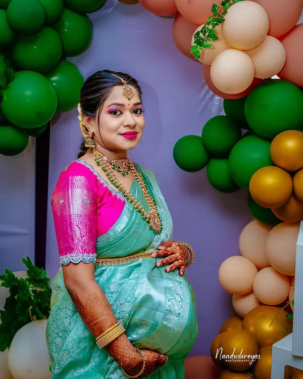 A close-up portrait of the radiant mother-to-be at her baby shower. Dressed in a beautiful traditional saree, she is glowing with happiness.