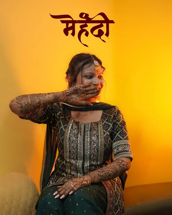 A shy smile and the beautiful fragrance of henna. This is a classic bridal portrait from a Mehendi ceremony, using warm lighting to highlight the bride's glow and the intricate henna design she's hiding with a playful hand.