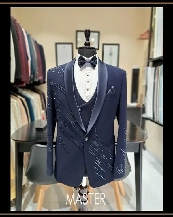 A three-piece navy blue tuxedo designed for a groom or groomsman. This suit features subtle, scattered embroidery on the jacket, adding a touch of sparkle to a classic silhouette.