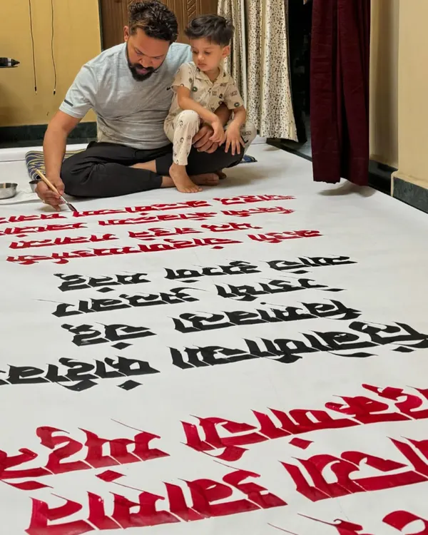 Working on a 15-foot long Marathi calligraphy paper roll for Gulmohar Day in Satara, with my son giving me company.