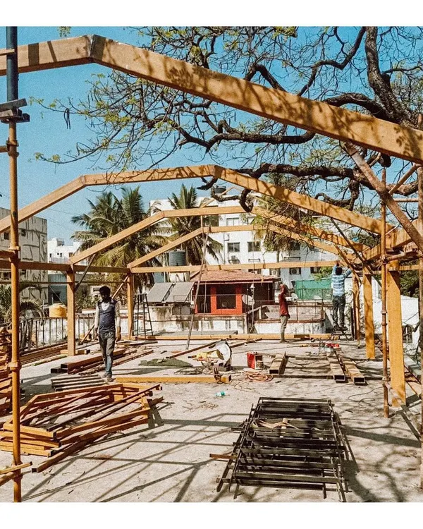 The initial construction phase of the rooftop conservatory, showing the assembly of the wooden frame under a large rain-tree. This image captures the raw beginning, where the architectural vision starts to take physical form.