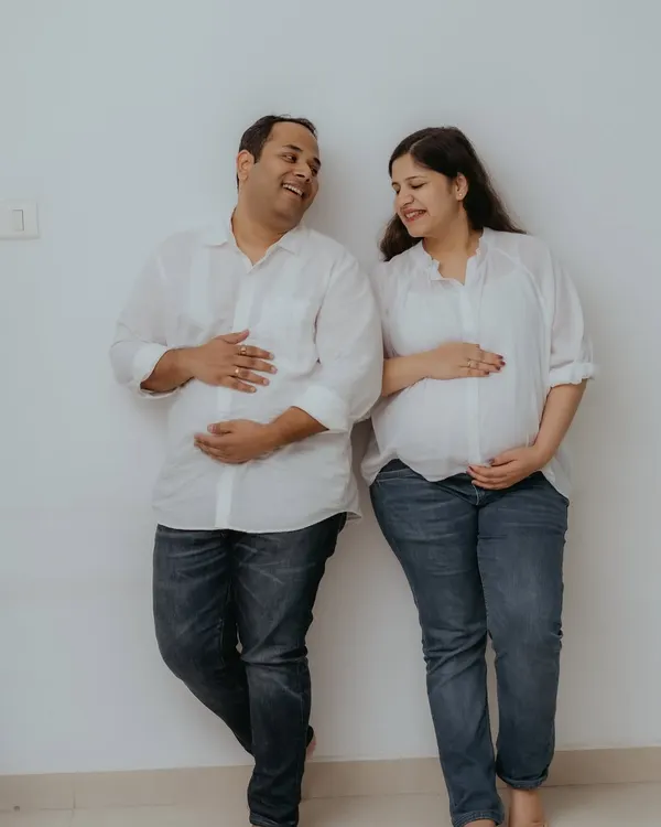 A fun and playful moment from a lifestyle home session, with both parents-to-be cradling their bellies. Dressed in matching casual white shirts and jeans, their shared laughter makes for a perfectly relaxed and joyful couple's maternity photo.