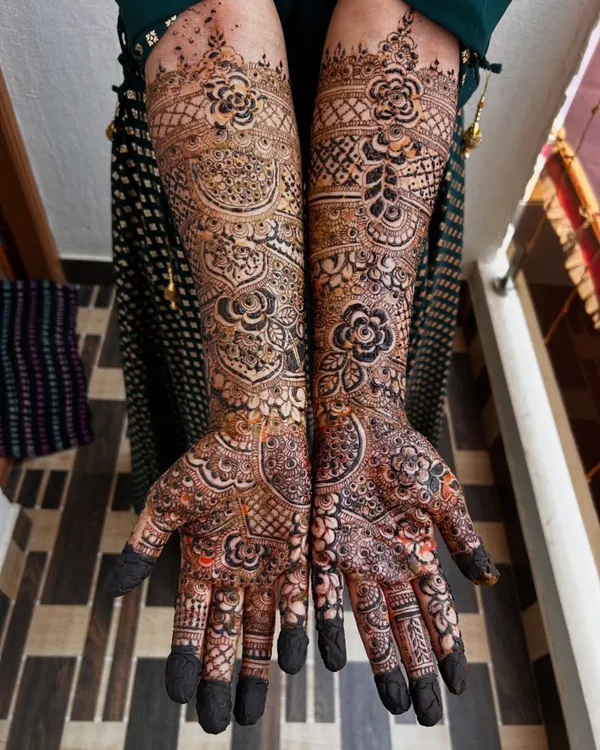 A stunning full-coverage bridal mehendi with a mix of floral and geometric patterns. Notice how the dark, filled-in flowers pop against the lighter, detailed background.