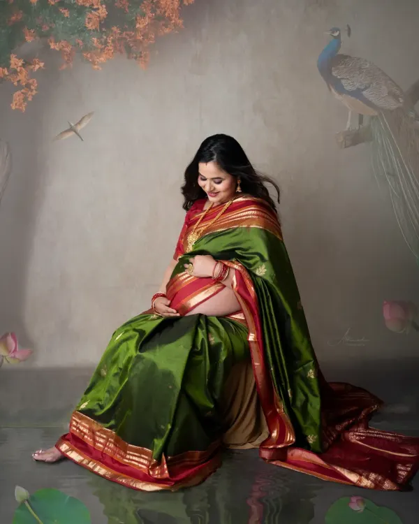 A portrait of traditional elegance. This mom-to-be looks absolutely stunning in a green and red silk saree, gently cradling her baby bump.