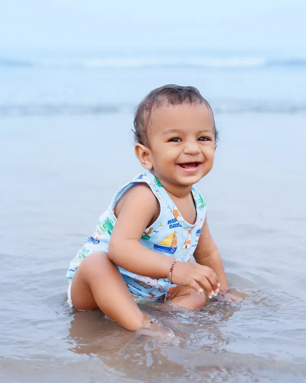 A baby boy's joyful smile as he sits in the shallow water at the beach. This is what pure, simple happiness looks like.
