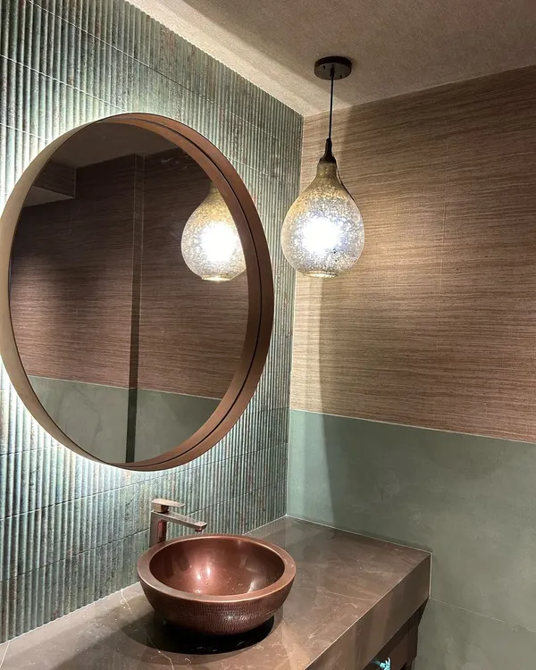 In this powder room, a palette of soft greens and browns creates a calming effect. The ribbed texture of the tiles, a hammered copper sink, and a mercury glass pendant light come together to form a space that is rich in texture.