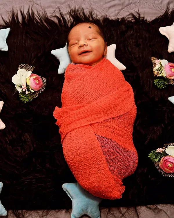 The sweetest smile from a sleeping baby, snugly wrapped in a red knit on a dark, furry blanket. The contrast makes the moment pop.