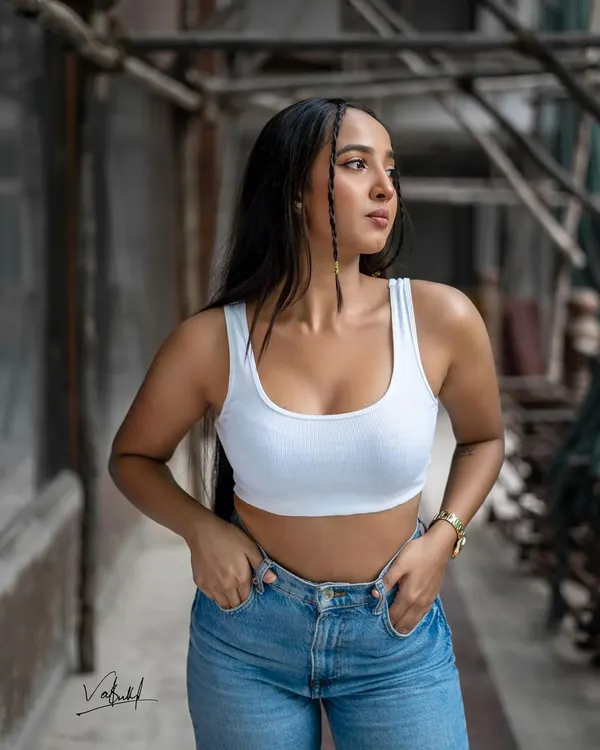 A candid-style street fashion shot, capturing a natural, off-the-cuff moment. The industrial background and the classic white tank and denim combination create a timeless and effortlessly cool look.