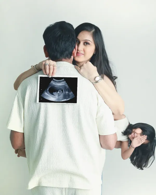 A creative and heartwarming pregnancy announcement. The family comes together to showcase the sonogram, with the older sibling peeking out playfully.