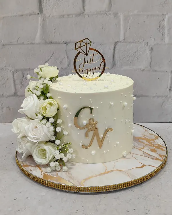 A classic and timeless engagement cake. This design features a clean white finish, a cascade of white roses, delicate pearl details, and a custom gold monogram for the happy couple.
