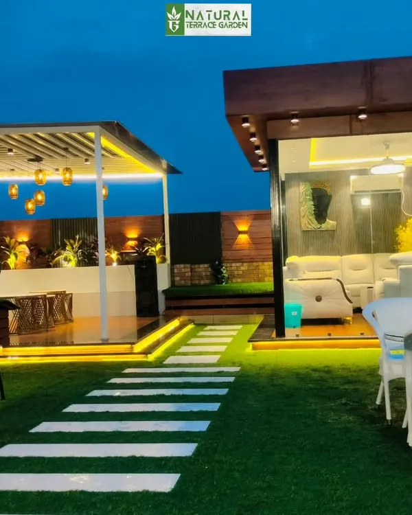 A complete rooftop transformation in Shahdara, New Delhi. This expansive terrace features a custom-built glass house, a modern pergola with integrated lighting, and a low-maintenance artificial lawn, creating a multi-functional outdoor living space perfect for evenings.