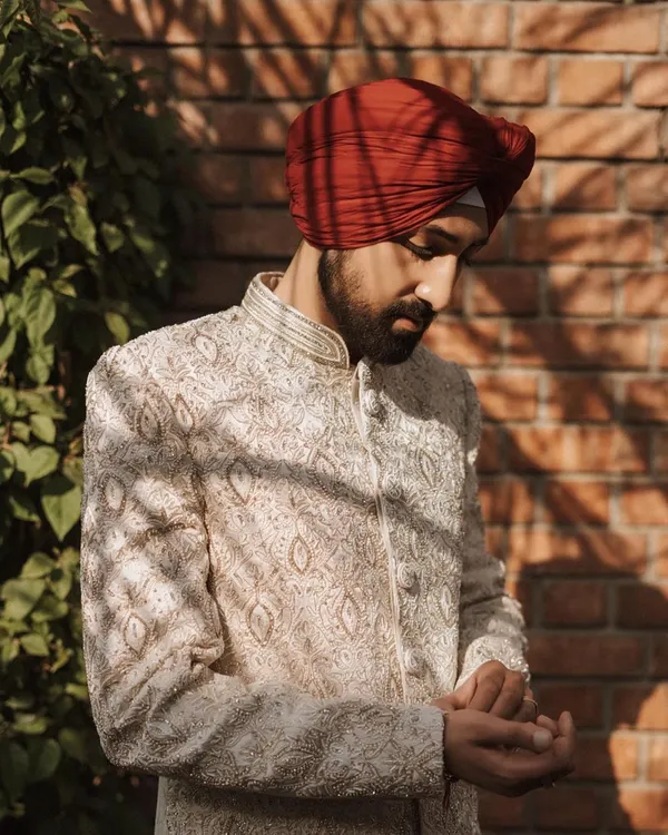 A groom adjusts his cuff, captured in warm sunlight against a brick wall. This is a classic, stylish portrait.