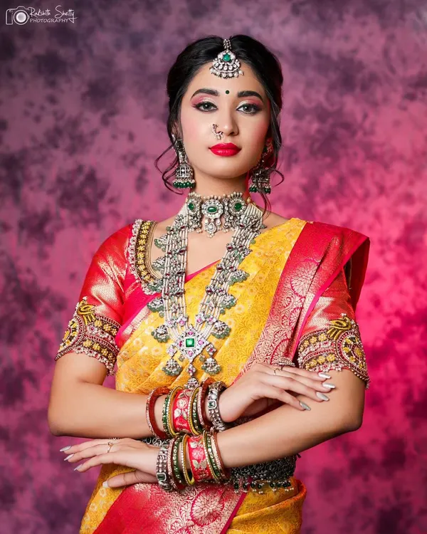 A studio portrait focusing on a model in a stunning yellow and red Kanchipuram silk saree. The focus is on the rich colors, heavy silver jewelry, and the model's confident and regal posture.