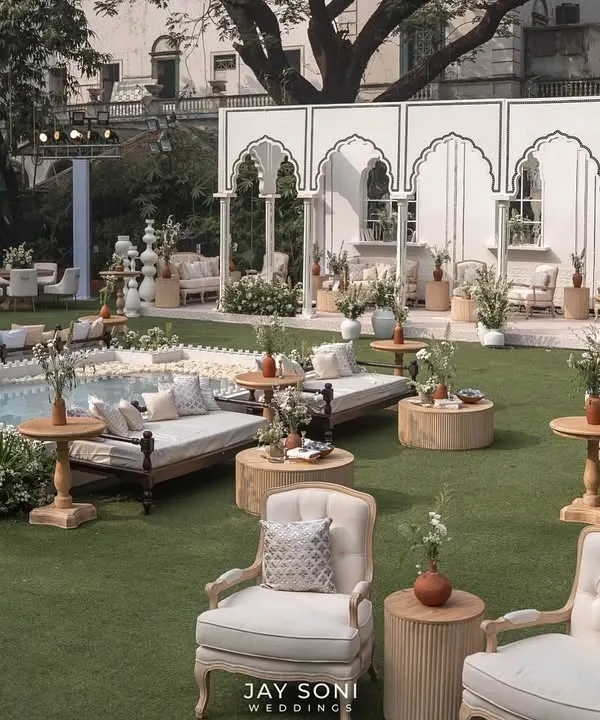 I designed this expansive outdoor lounge to feel like a luxurious garden retreat. The space features a mix of classic upholstered armchairs, traditional daybeds, and a serene water feature, all unified by a chic ivory and white color palette.