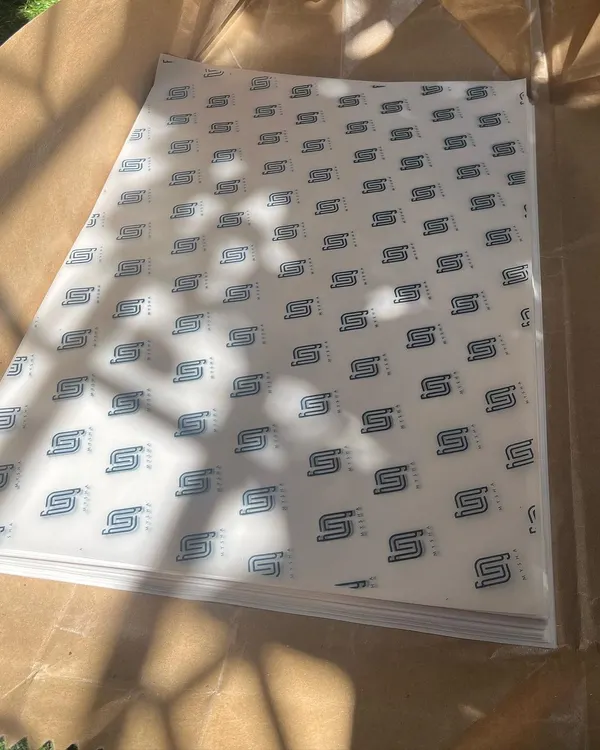 A stack of freshly printed custom wrapping paper for the clothing brand Mysha. A repeating logo pattern creates a strong, professional brand impression right from the packaging.