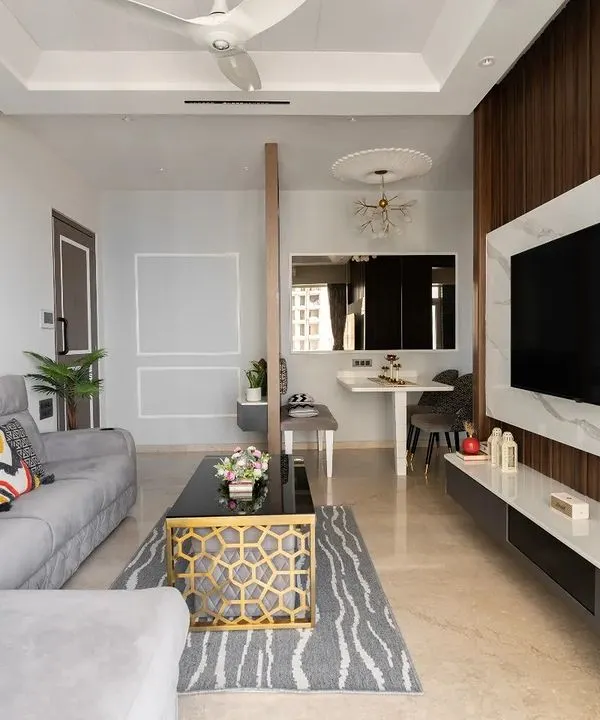 This living room combines a comfortable grey sectional sofa with a stunning TV unit featuring a marble-finish backdrop and wood fluting. The design is minimalist yet full of texture and warmth, perfect for a modern family. This is the wide shot of the space.