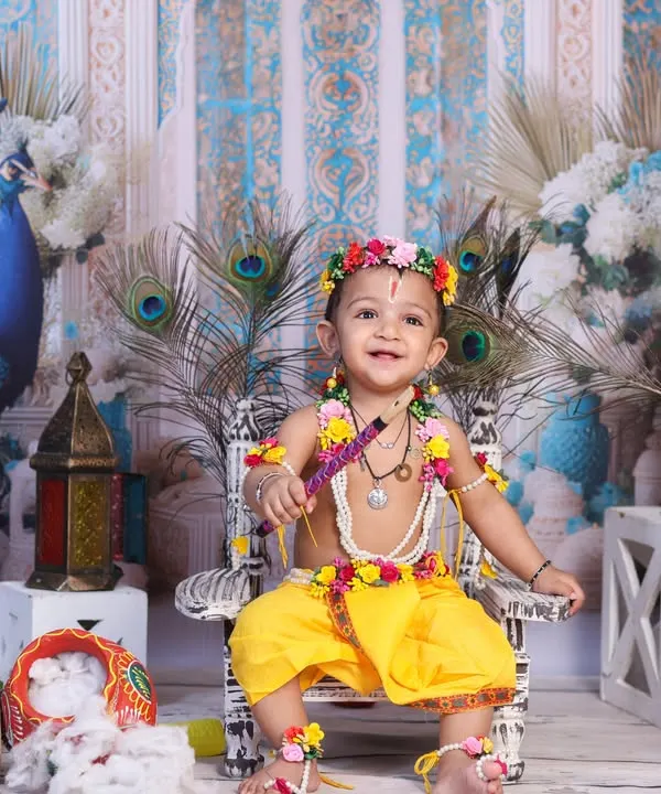 A joyful Little Krishna, smiling brightly while seated on a miniature throne adorned with peacock feathers. This setup is perfect for capturing your baby's happy spirit during Janmashtami.