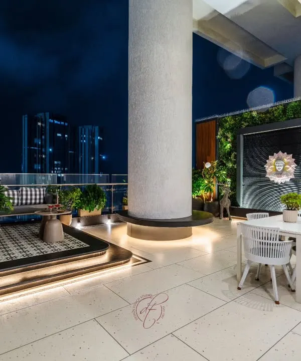 This luxurious rooftop terrace is an urban oasis. It features a raised seating area, a separate dining space, and a stunning Buddha water feature set against a vertical garden, all with a breathtaking view of the city at night.