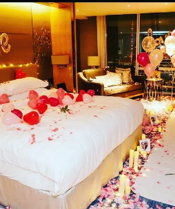 A complete romantic room transformation for a special anniversary. I used a trail of rose petals and flameless candles leading to the bed, which is decorated with heart-shaped balloons and a 'LOVE' foil banner for a truly memorable surprise.