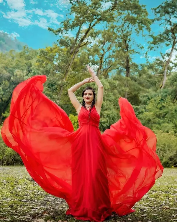 A dramatic outdoor fashion portrait captured in a lush, green landscape. The movement of the vibrant red flowing gown creates a powerful and epic image, perfect for a pre-wedding shoot or an editorial fashion portfolio.