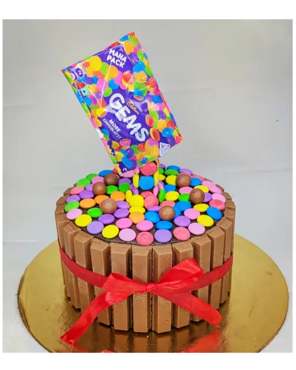 An anti-gravity Gems explosion cake that's as fun to look at as it is to eat. This is a chocolate truffle cake surrounded by KitKat bars, with colorful Gems pouring out of the bag.