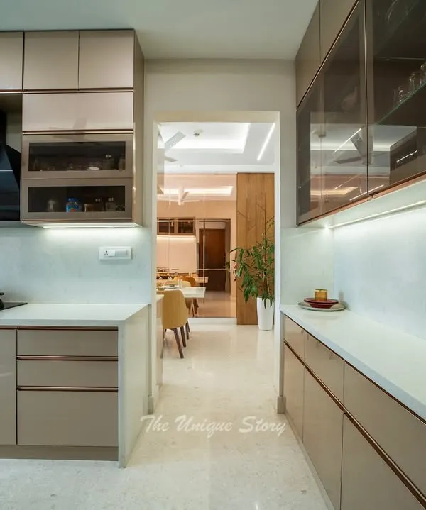 This modern kitchen is designed for a clean and calm aesthetic, featuring glossy, handle-less beige cabinets and a white quartz countertop. The view opens into the dining area, showcasing the open-concept layout that connects the spaces.
