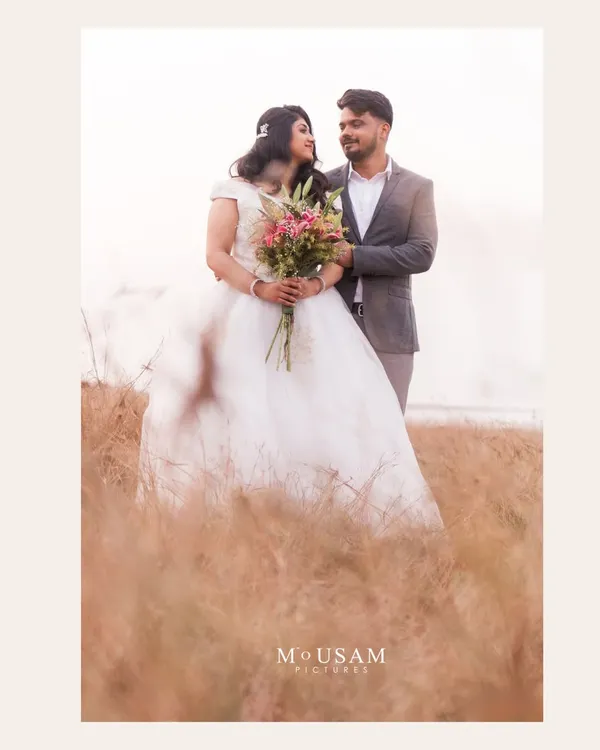 A classic, romantic portrait in a field of golden grass. She holds a bouquet as he stands beside her, their gazes meeting in a moment of sweet connection. The soft light creates a dreamy, fairytale atmosphere.