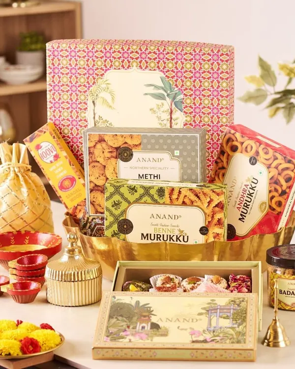 This grand festive hamper is a true celebration, overflowing with boxes of Anand methi mathi and murukku, a jar of badamika, and a selection of sweets, all beautifully arranged in a large, ornate basket.