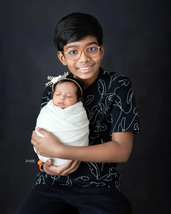 A proud big brother holding his newborn sister. I use a simple, dark background to create a classic and timeless sibling portrait that focuses on their bond.