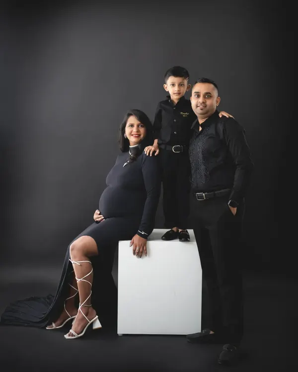 A fun and stylish family portrait in matching black outfits. The older brother stands proudly on a block, excited about his promotion.