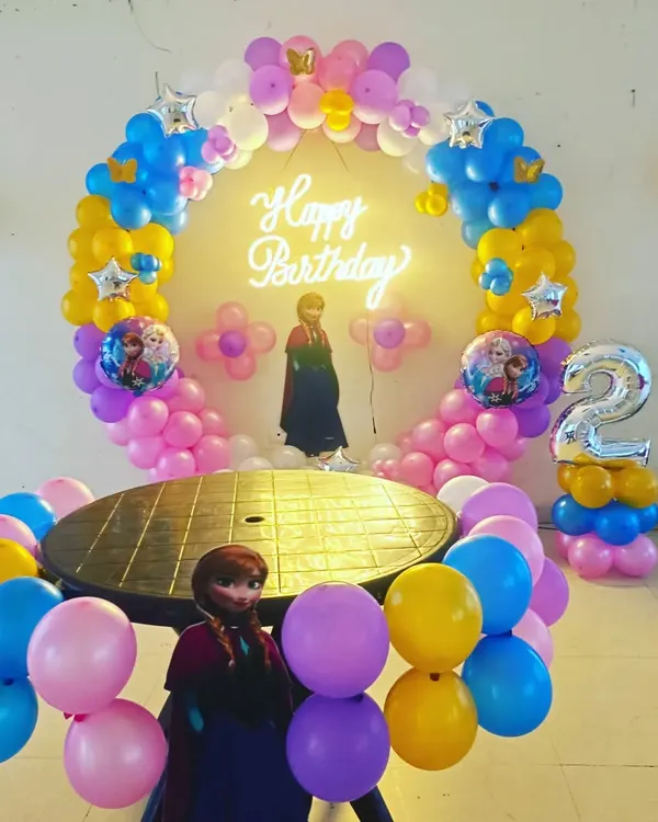 Yeh Frozen theme par second birthday party ki decoration hai. Ismein humne Anna aur Elsa ke cutouts, theme ke color ke balloons ka ring, aur '2' number ka foil balloon use kiya hai.