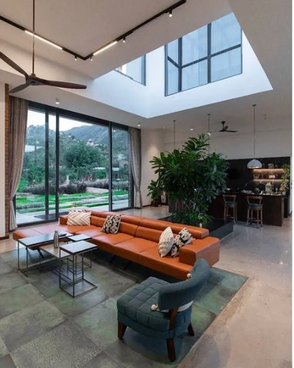 This living room from our Weekend Home at Nandi Hills captures our core philosophy. We designed it with floor-to-ceiling windows and a central skylight to flood the space with natural light, blurring the line between indoors and the beautiful landscape outside. The open-plan layout, featuring an indoor planter and views of the hills, creates a seamless connection with nature.