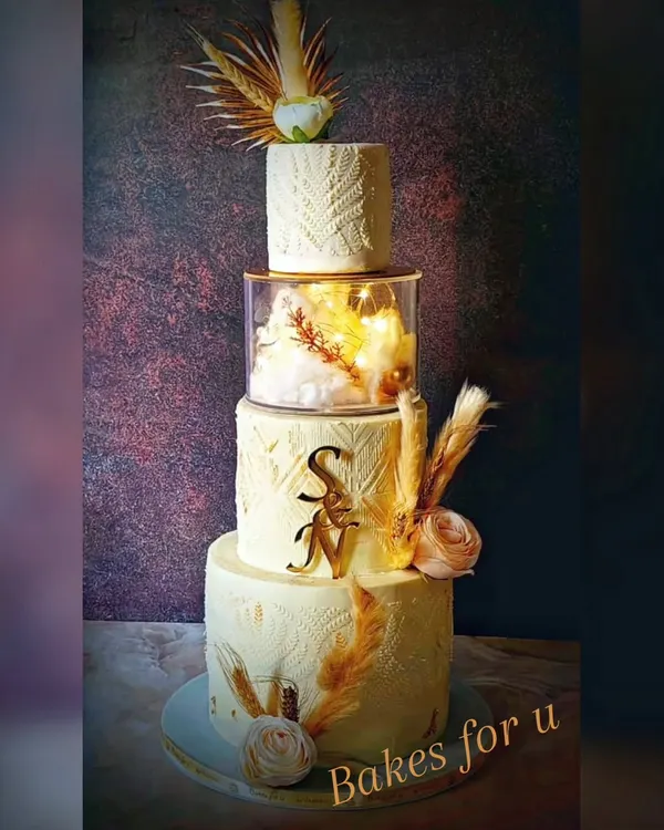 A beautiful four-tier wedding cake with a rustic, bohemian theme. The design features textured buttercream, dried pampas grass, and the couple's initials for a personal touch.