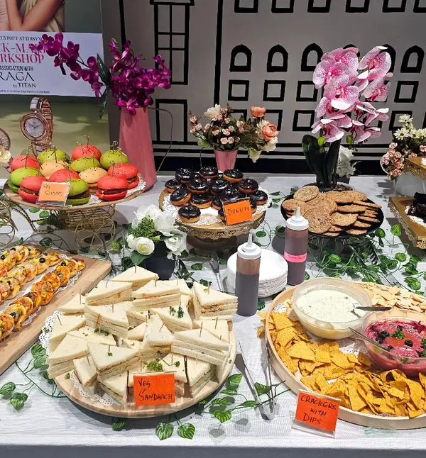 A full view of our stunning hi-tea grazing table set up for a workshop at a Bangalore shopping mall. It features an abundant spread of sandwiches, macarons, donuts, nachos with dip, and more.