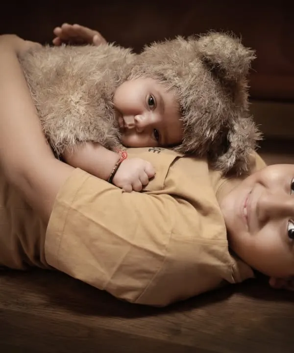 The beginning of a lifelong friendship. This tender moment shows an older brother lovingly cuddling his new baby sibling, who is dressed in an adorable bear costume.