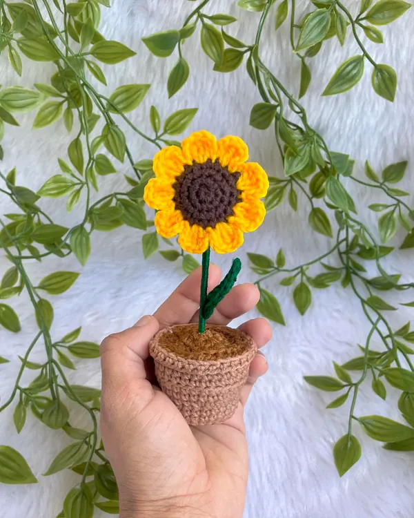 A tiny, adorable potted sunflower held in my hand. This little plant is perfect for adding a touch of handmade charm to any small space.