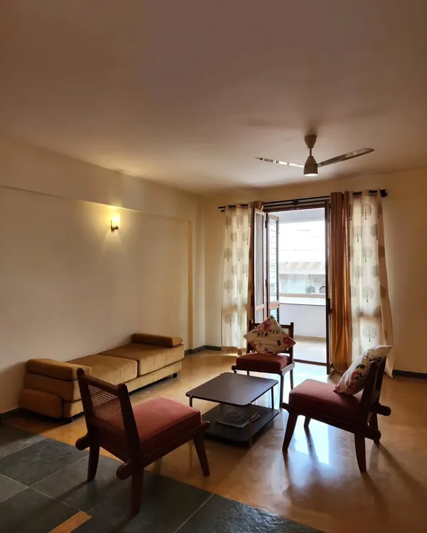 A simple, warm living room in a residential apartment. The design uses a minimal palette of wood and neutral tones, with an open connection to the balcony to maximize light and space.