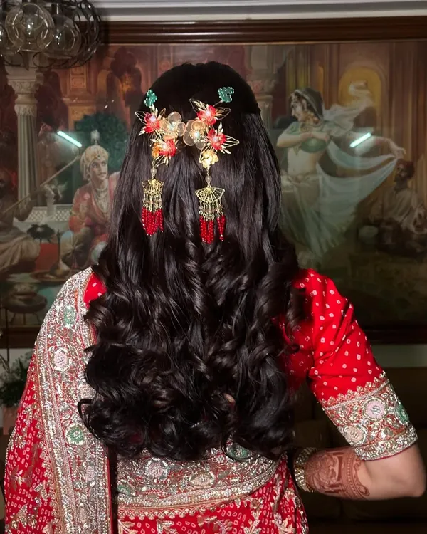 A beautiful half-updo with soft curls, adorned with ornate, dangling hair accessories. This hairstyle is perfect for a Sangeet or wedding ceremony, adding a touch of royalty to the look.