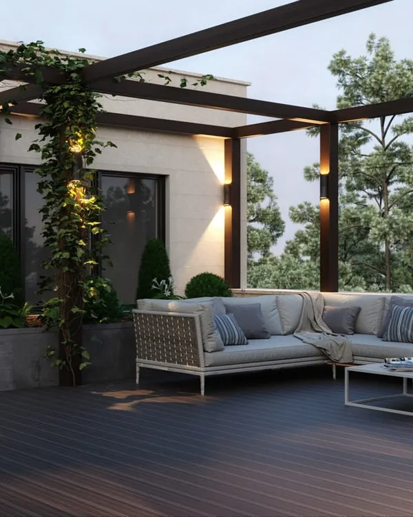 This view of the rooftop terrace highlights the lighting design, with warm uplights on the pergola columns creating a beautiful ambiance at dusk. The L-shaped sofa provides ample seating, making it an ideal space for evening gatherings.
