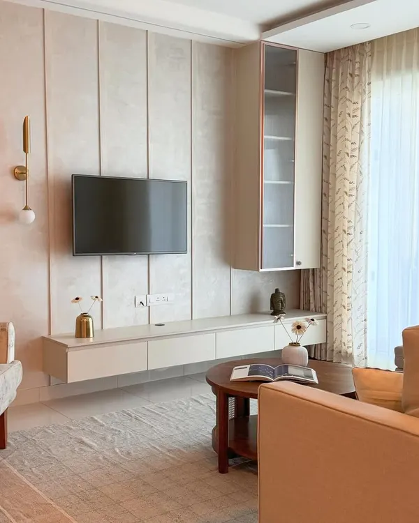 A living room that whispers elegance. The design uses soft beige tones, a floating TV unit with metallic accents, and warm lighting to create a serene, light-filled retreat.