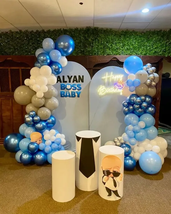 The Boss Baby has arrived! This stylish birthday setup features two backdrops, custom-printed pedestals, a neon "Happy Birthday" sign, and a cool blue, white, and silver balloon garland.