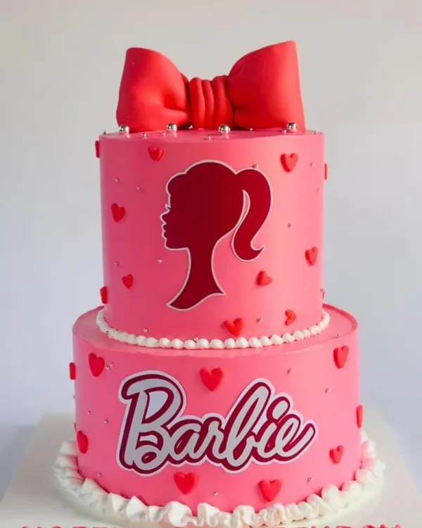 A classic two-tier Barbie cake in pink, featuring the iconic silhouette and a big red bow.