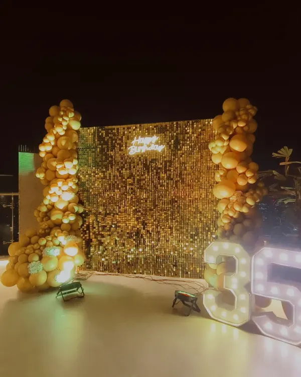 A glamorous 35th birthday setup. The glittering gold sequin wall, 'Happy Birthday' neon sign, and large light-up marquee numbers create a perfect photo spot for celebrating a major milestone.