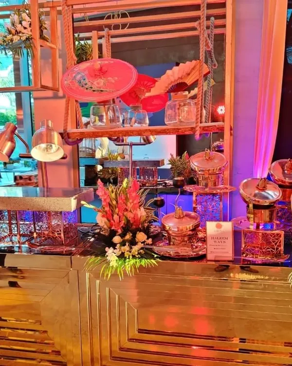A wide view of our modern buffet setup featuring a geometric gold-mirrored counter. The station is decorated with floral arrangements and uses our signature copper chafing dishes, creating a luxurious look for a wedding.